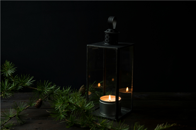 Lighted candle inside black lantern holder by Joanna Kosinska